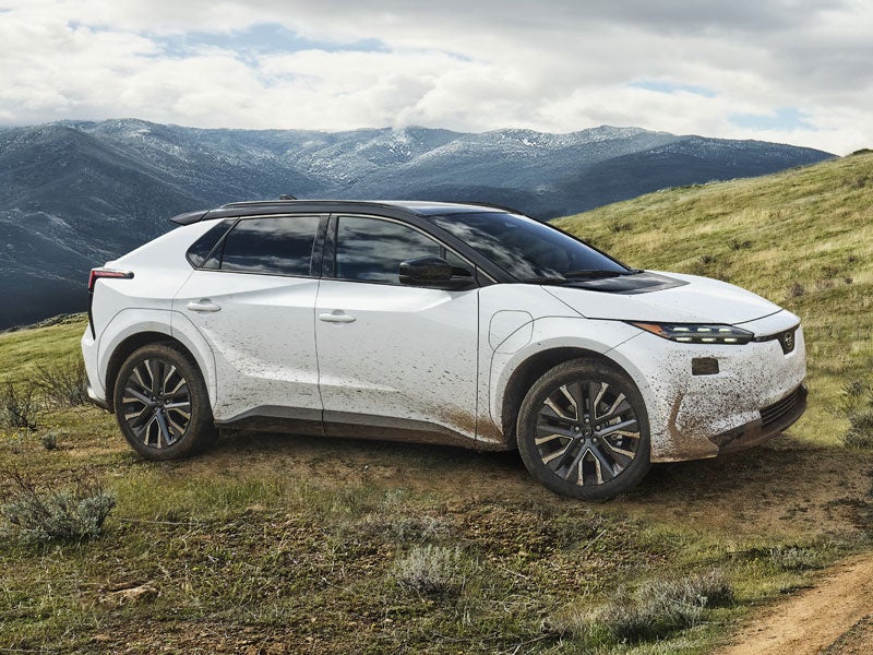 A static image of a white 2027 Subaru Solterra parked on a grassy hill.