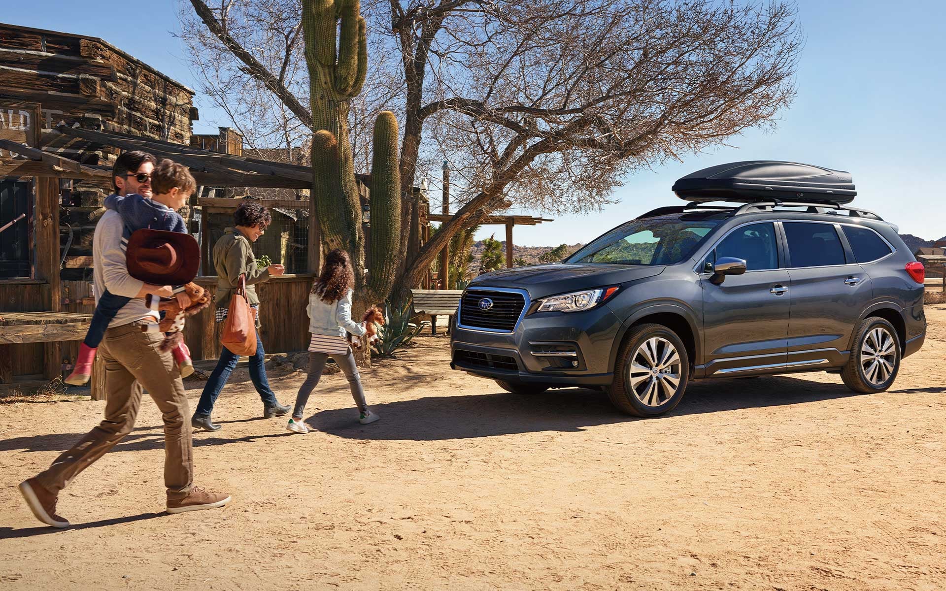 Family of four walks in a desert town toward their charcoal gray SUV with a black rooftop cargo box.