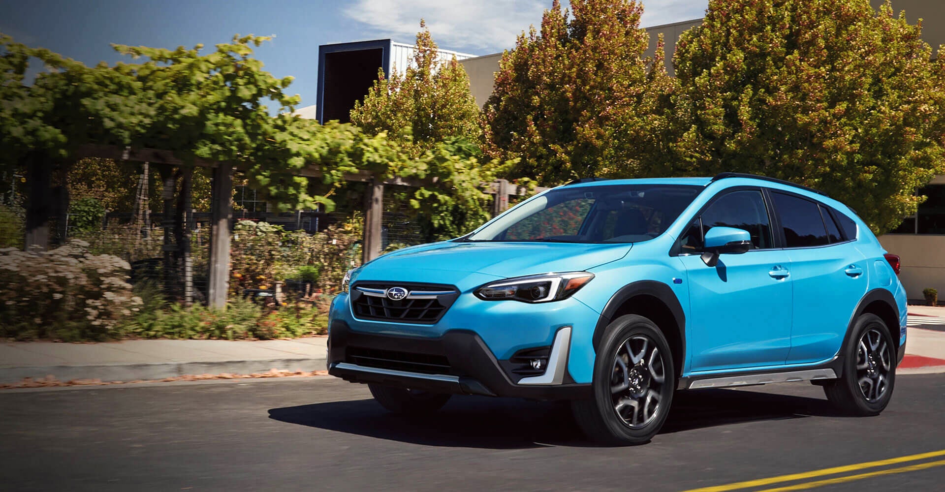 A bright blue Subaru Crosstrek SUV driving down a road with trees and foliage in the background.