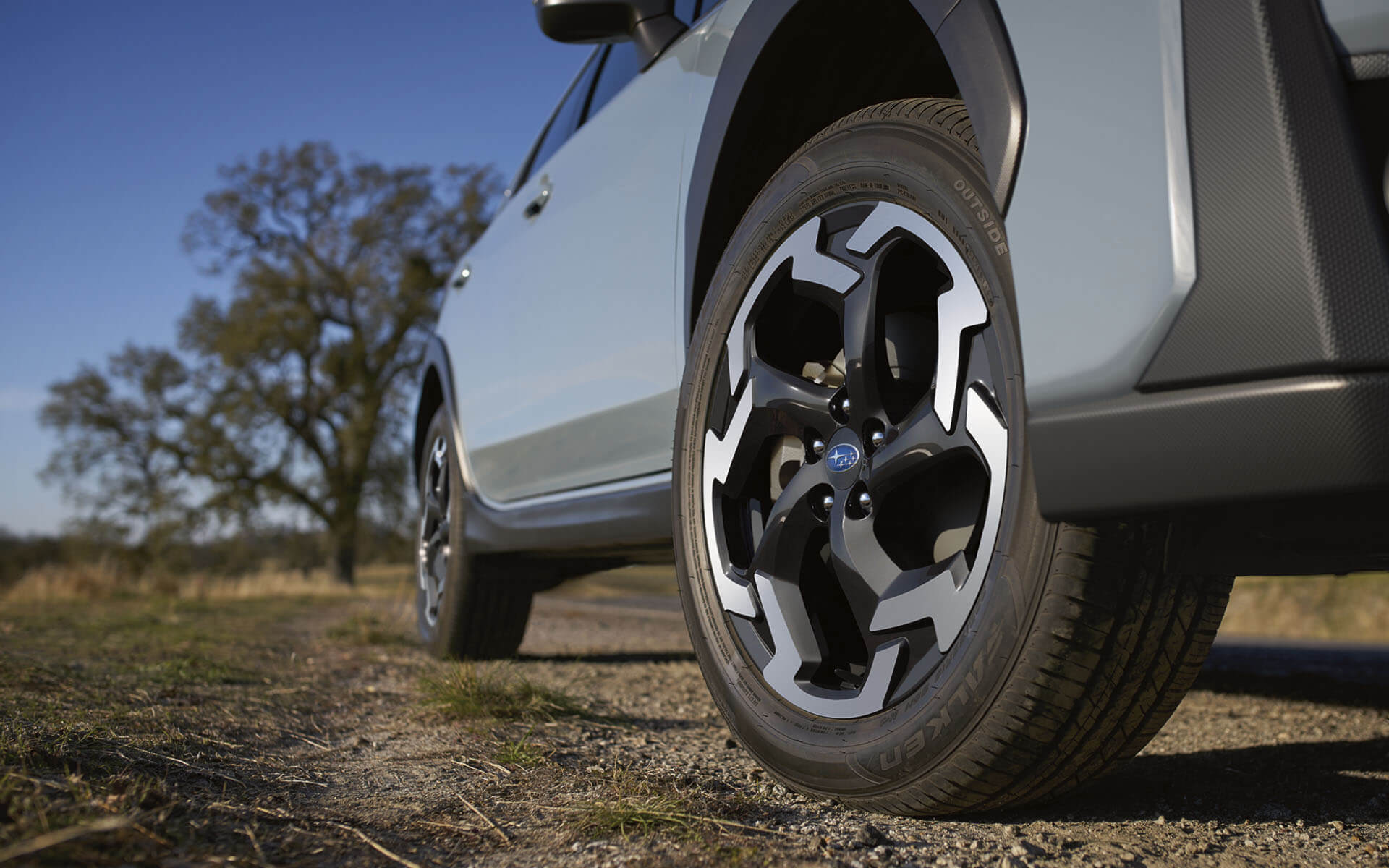 A light-colored Subaru Crosstrek SUV, seen from the front passenger side, parked on a gravel path.