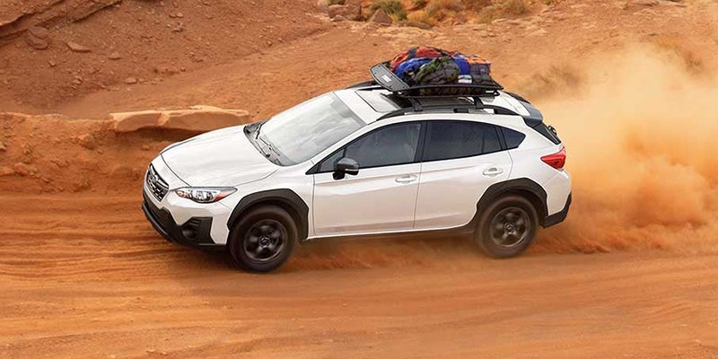 White SUV with a rooftop cargo carrier kicks up an orange dust cloud on a dirt road.
