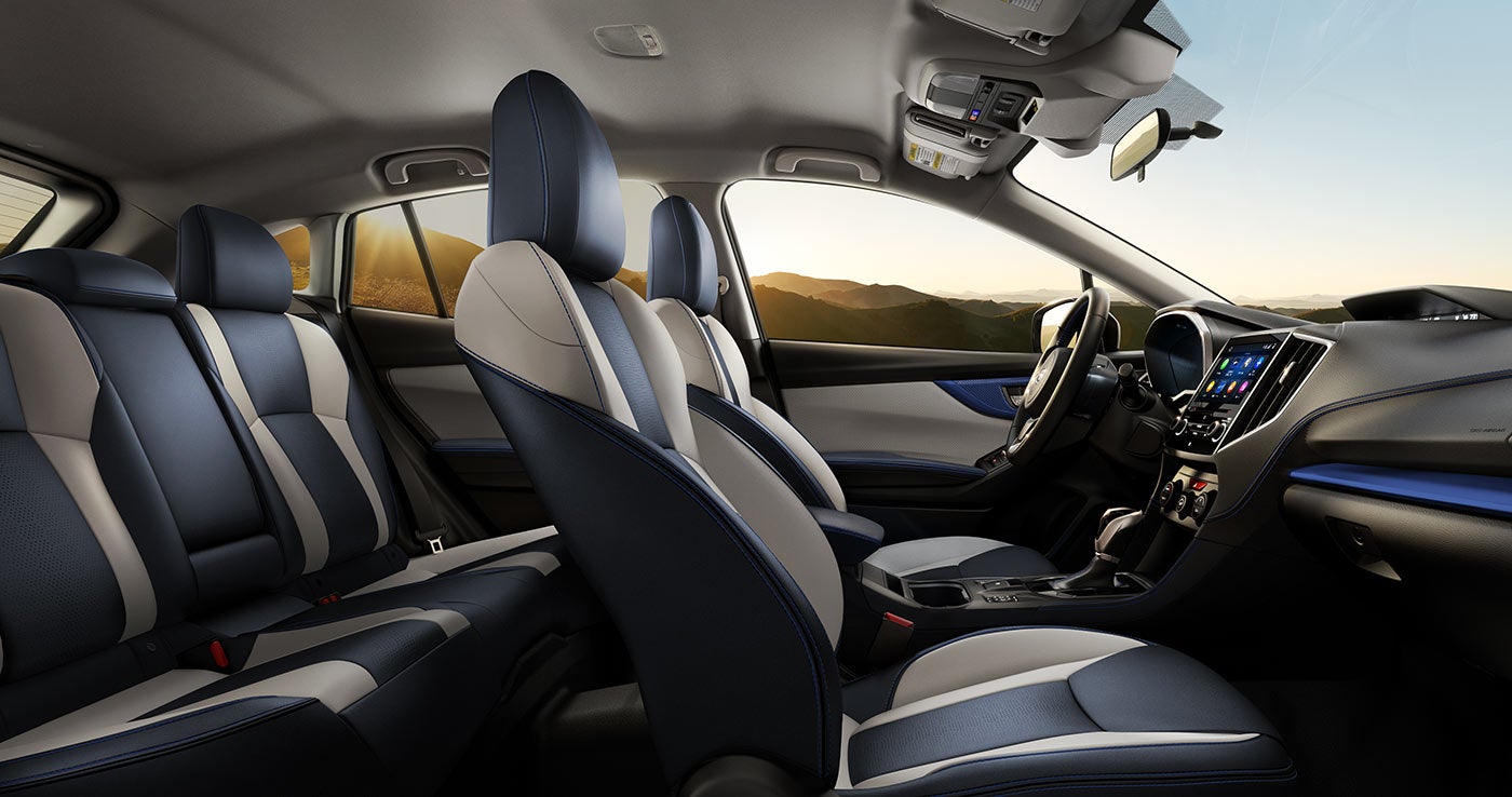 Interior view of a car with dark blue and beige seats, dashboard touchscreen, and a sunset over mountains through the windows.