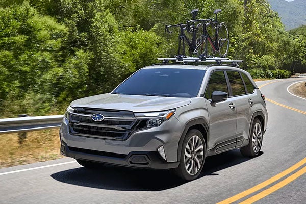 A silver Subaru Forester driving on a paved road with two bicycles mounted on a roof rack