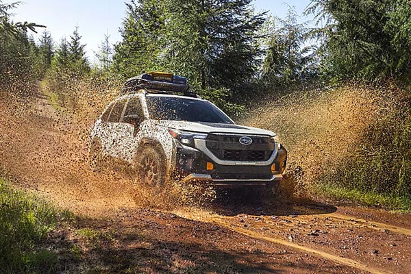 A Subaru Forester splashing mud while driving off-road through a forested trail.