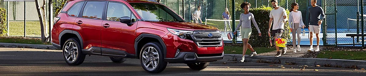 A red Subaru Forester parked near tennis courts with people walking nearby carrying gear.
