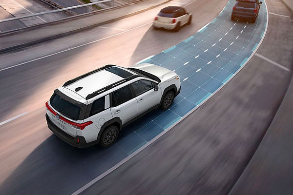 Aerial high-angle shot of a white Subaru Outback driving on a highway, demonstrating lane-centering and safety sensor technology graphics.