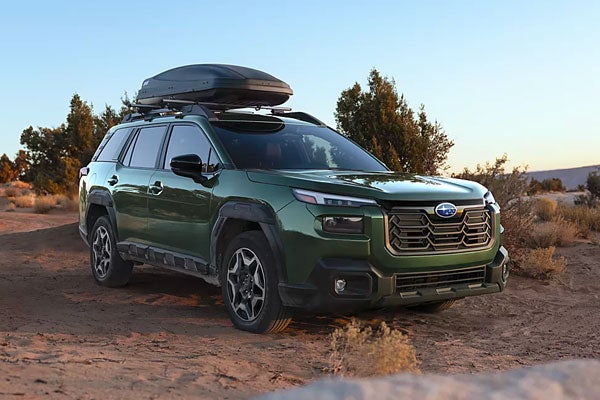 Green Subaru Outback parked on an off-road dirt path equipped with a roof cargo carrier.