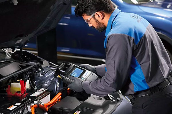 Factory-trained Subaru technician inspecting vehicle engine with diagnostic tool