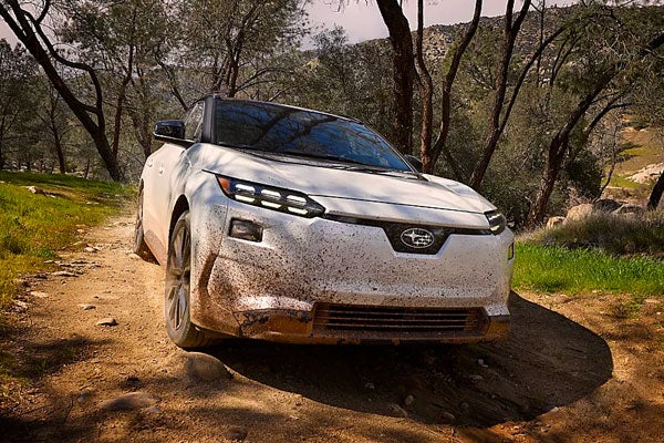 Front view of a dirty white Subaru Solterra driving along a dirt off-road trail.
