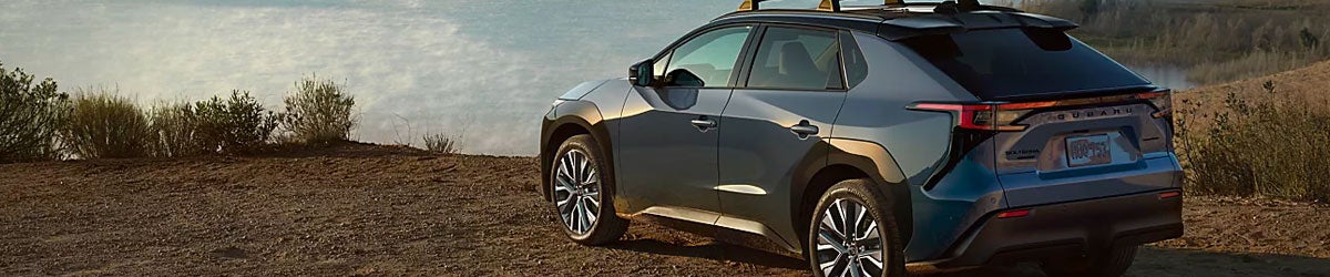 Rear three-quarter view of a blue Subaru Solterra parked on an overlook path with scenic mountains in the background.