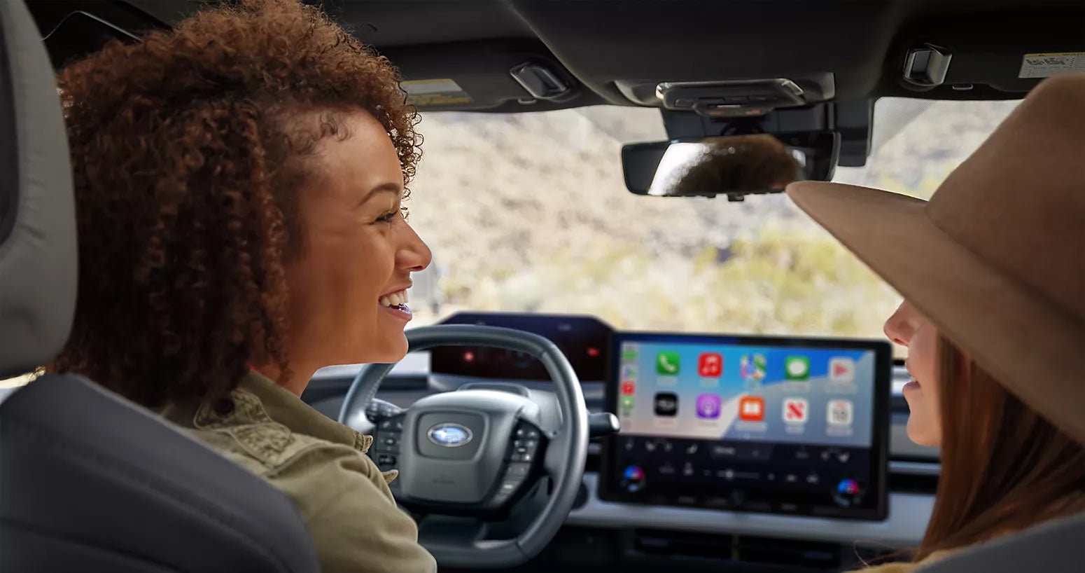 A view from the rear passenger seat of two people talking in a Subaru cabin.