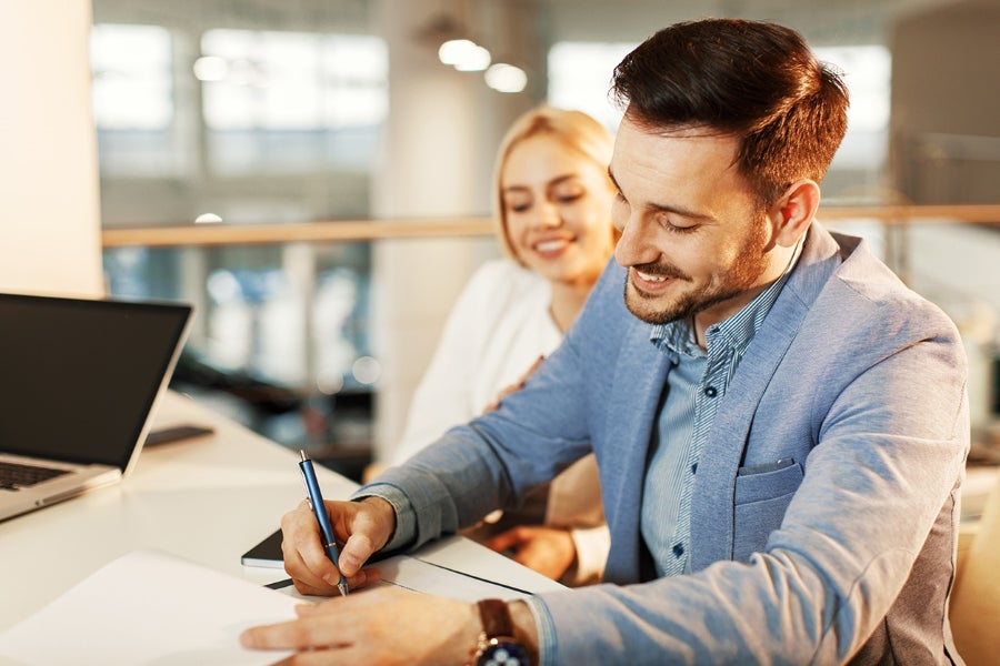 A photo of a man signing paperwork inside of a dealership.