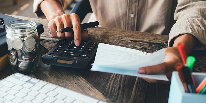 A closeup shot of a person using a calculator on a wooden desk.