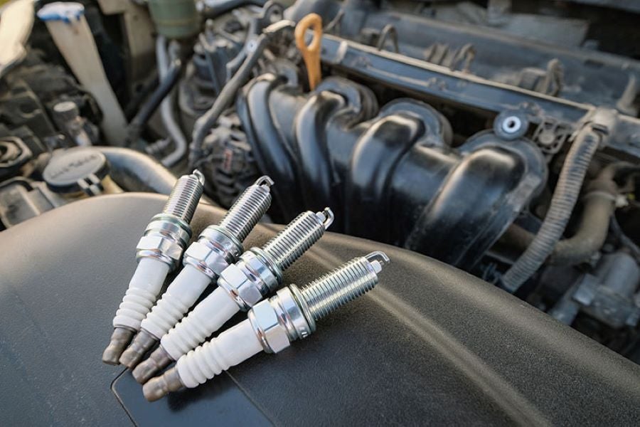 Four new spark plugs resting on a dark car engine cover.